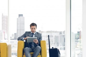 Businessman sitting in a chair and waiting for a meeting or plane, using a digital tablet.