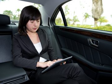 Young businesswoman sitting in her car using a digital tablet.